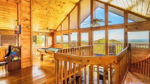 A wooden cabin interior with a pool table, a ceiling fan, and large windows offering a view of the outdoors. - Panoramic Views w/ Hot Tub, Pool Table, Arcade! (Sevierville)