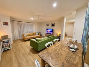 A living room with a wooden dining table, a green sofa, a beige sofa, a television, and a ceiling fan. - Booyun@Bruns - 2 bedroom apartment - walk to shops, river and beach (Brunswick Heads)
