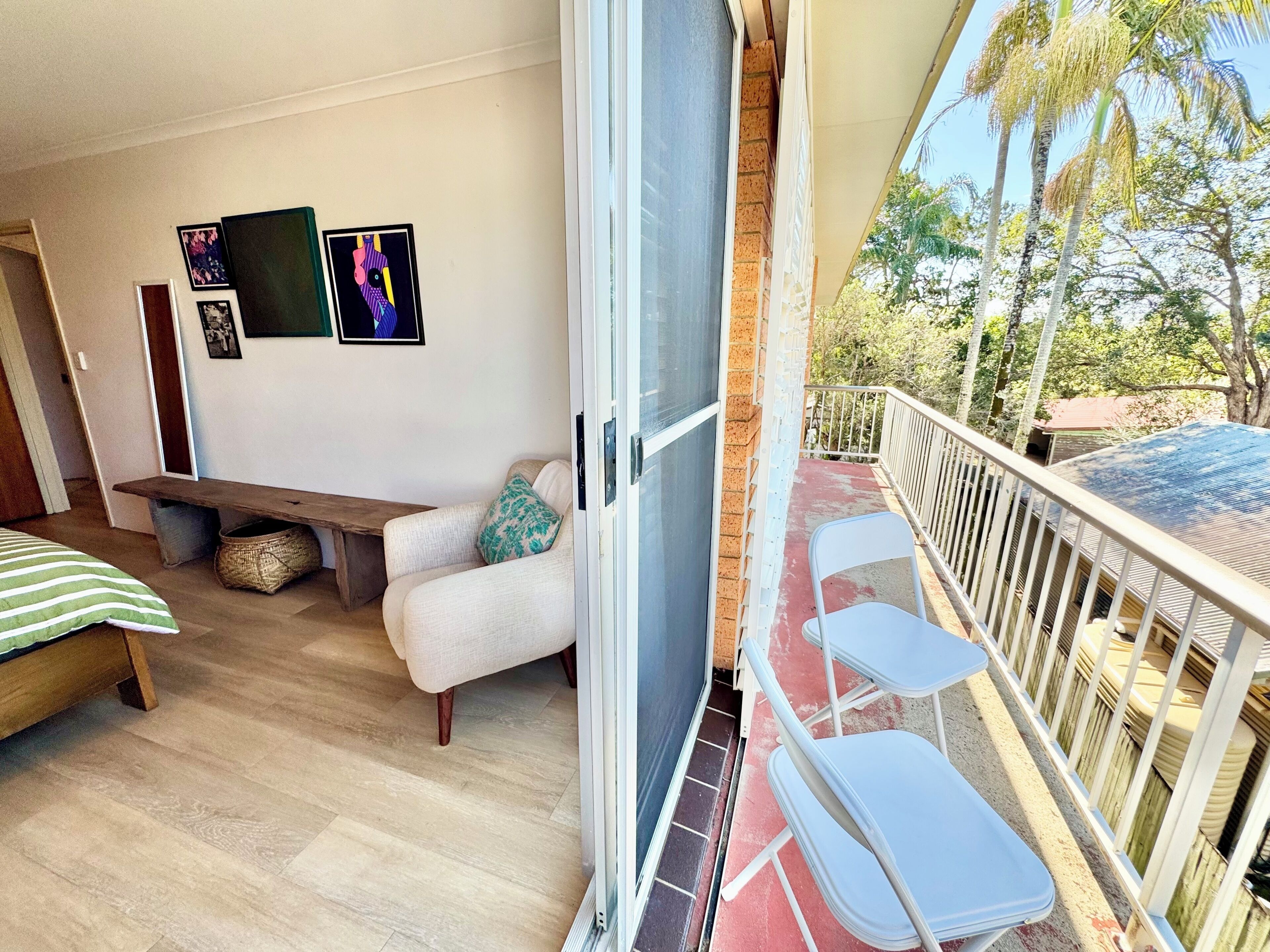 A balcony with a wooden floor, a white sofa, a bench, and a white chair.