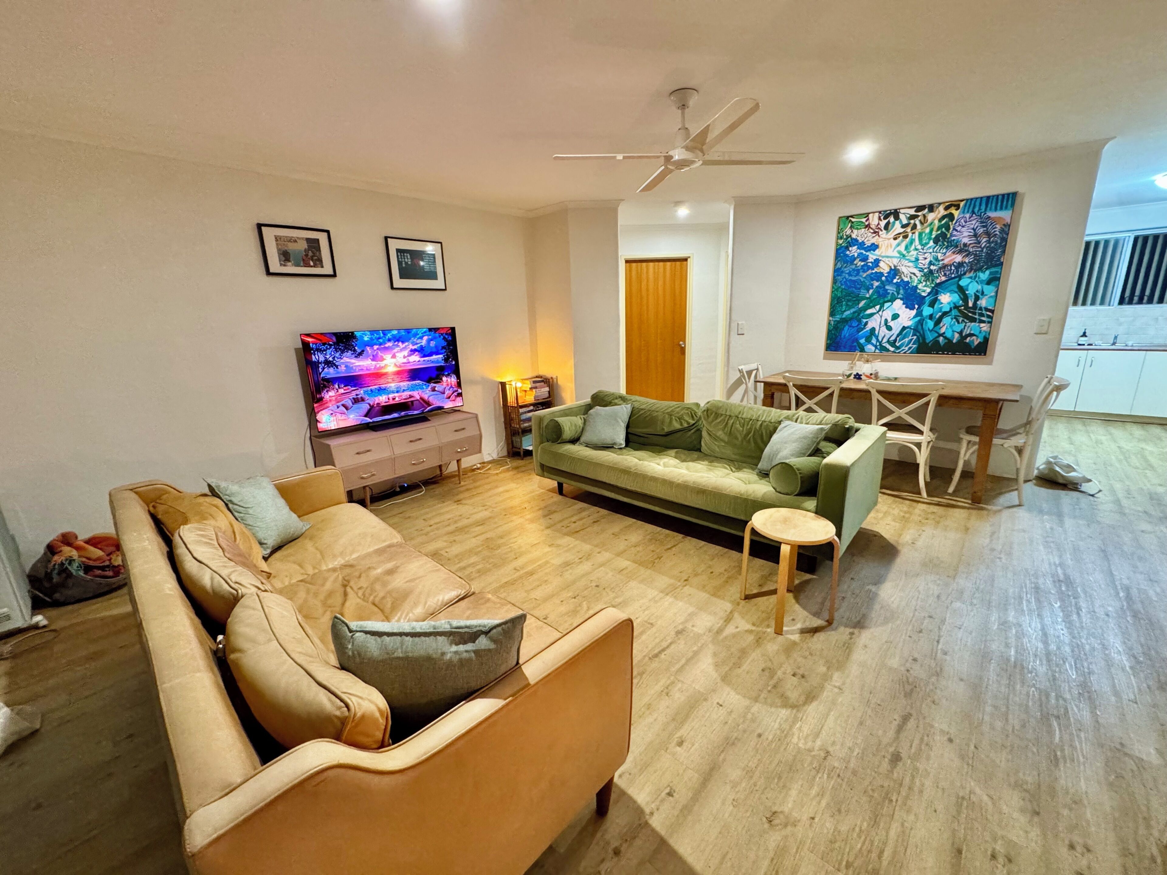 En stue med tv, to sofaer, et spisebord og en loftsvift.
