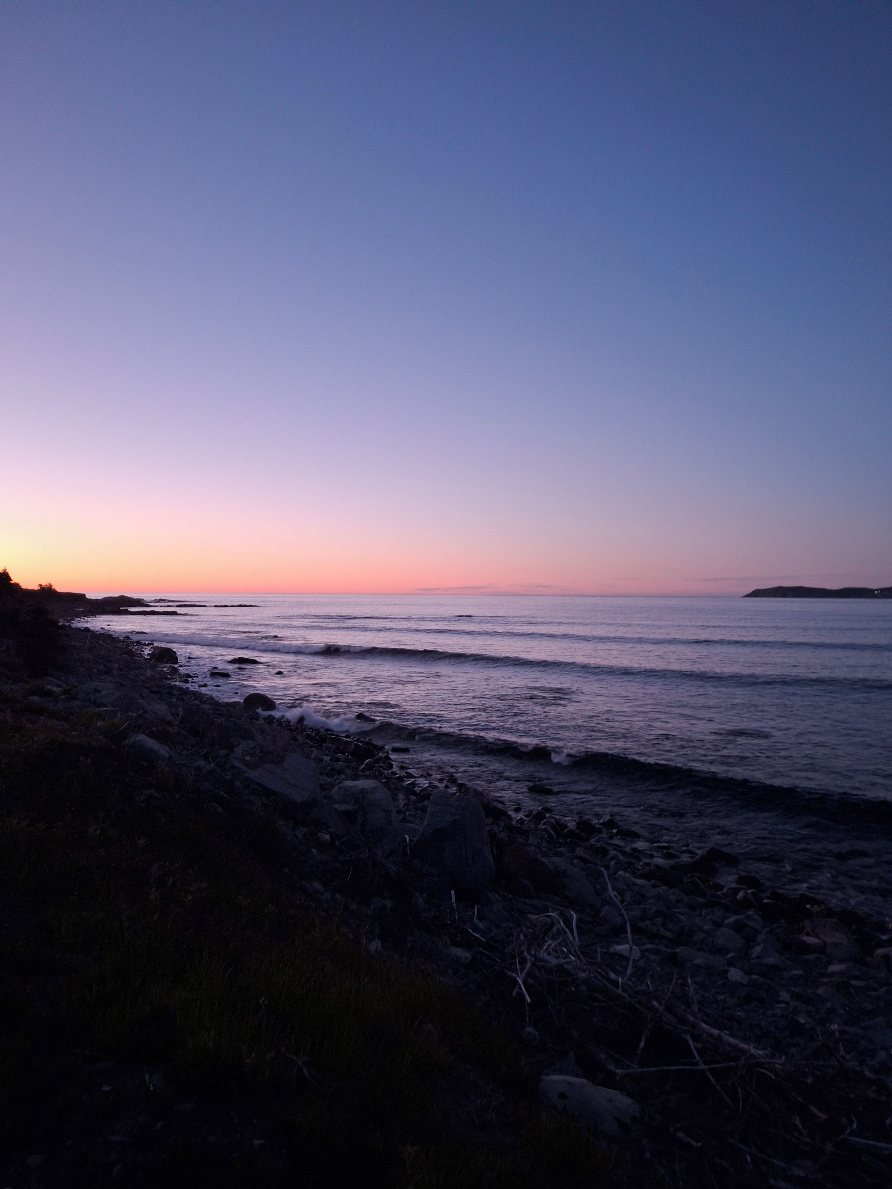 A coastal landscape with a rocky shoreline and calm sea during twilight.