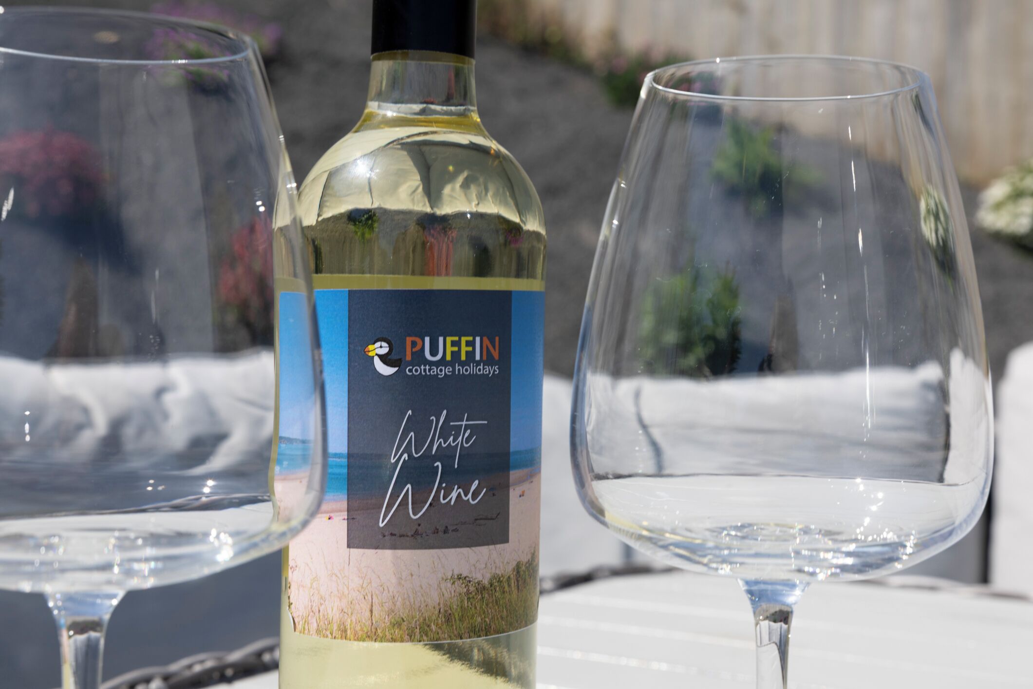 Une bouteille de vin blanc de la marque Puffin Cottage Holidays et deux verres à vin vides sur une table.