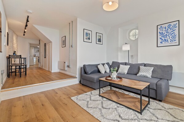 Een moderne woonkamer met een grijze bank, een houten salontafel en een kamerkleed met een patroon.