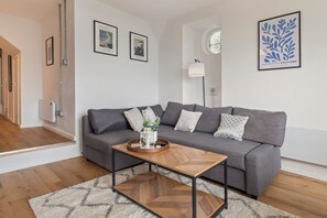 Een moderne woonkamer met een grijze bank, een houten salontafel en een kamerbreed tapijt met een patroon.
