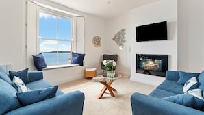 Ein Wohnzimmer mit einer Couch, einem Glastisch, einem Kamin, einem Fernseher und einem Fenster mit Aussicht.