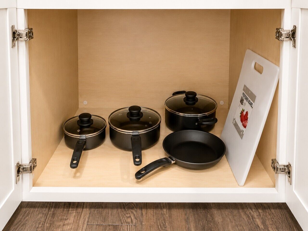 A kitchen cabinet with four black pots and pans, a whiteboard, and a door handle.