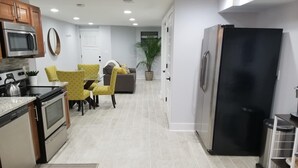 A modern kitchen with stainless steel appliances, a dining area with yellow chairs, and a living room with a gray sofa. - Private DC Apartment - 1BR - Walk to Metro - Explore Washington DC (Washington)