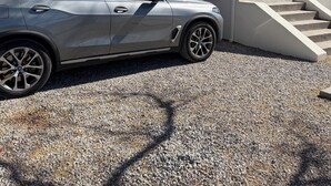 Ett hus med en grusuppfart, en bil parkerad framför och en trappa som leder upp till entrén.