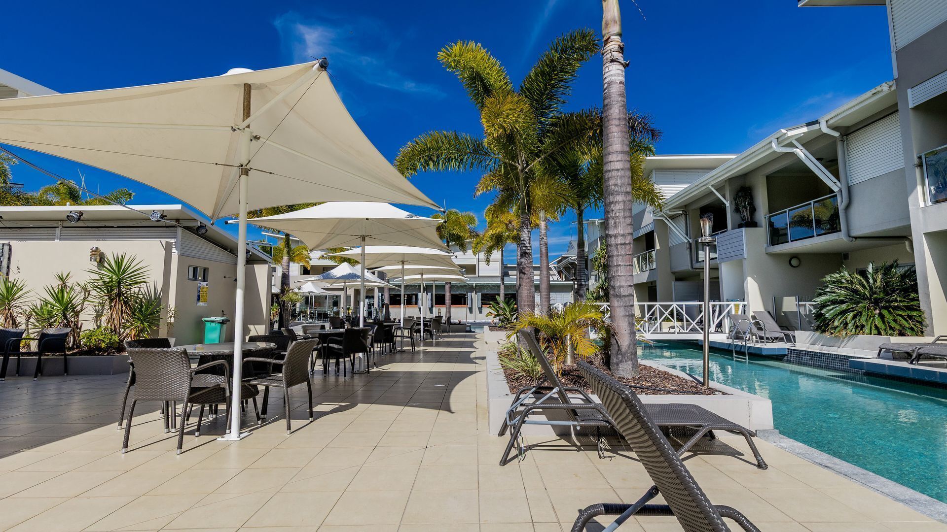 Un resort con mesas al aire libre, piscina y palmeras.