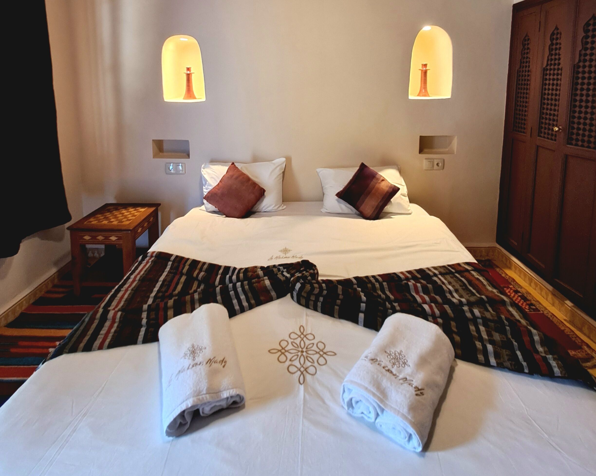 A hotel room with a bed, two bedside lamps, a nightstand, and a patterned carpet.