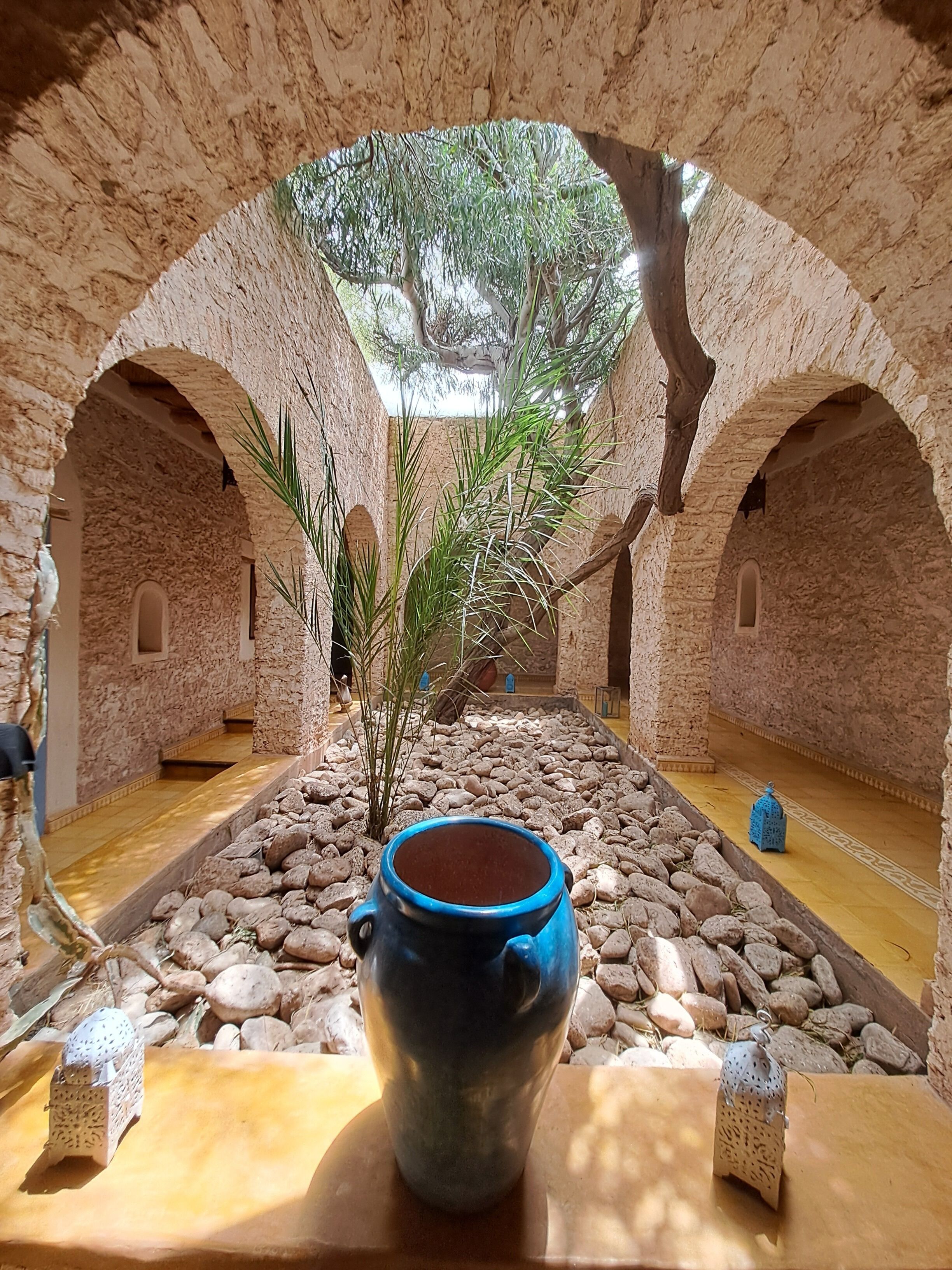 An interior courtyard with stone arches, a central water feature, and a blue pot on a table.