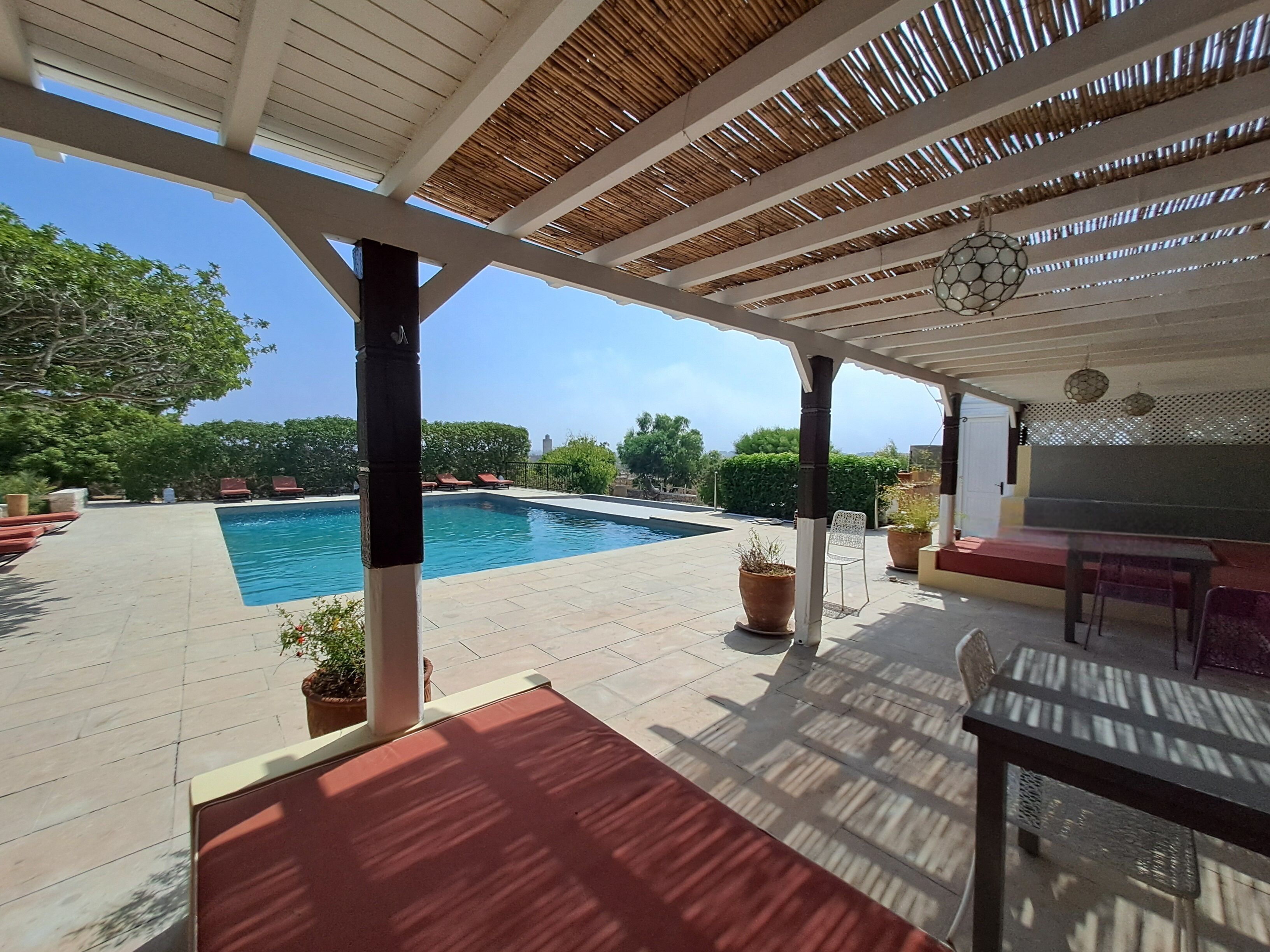 A covered outdoor area with a pool, seating, and potted plants.