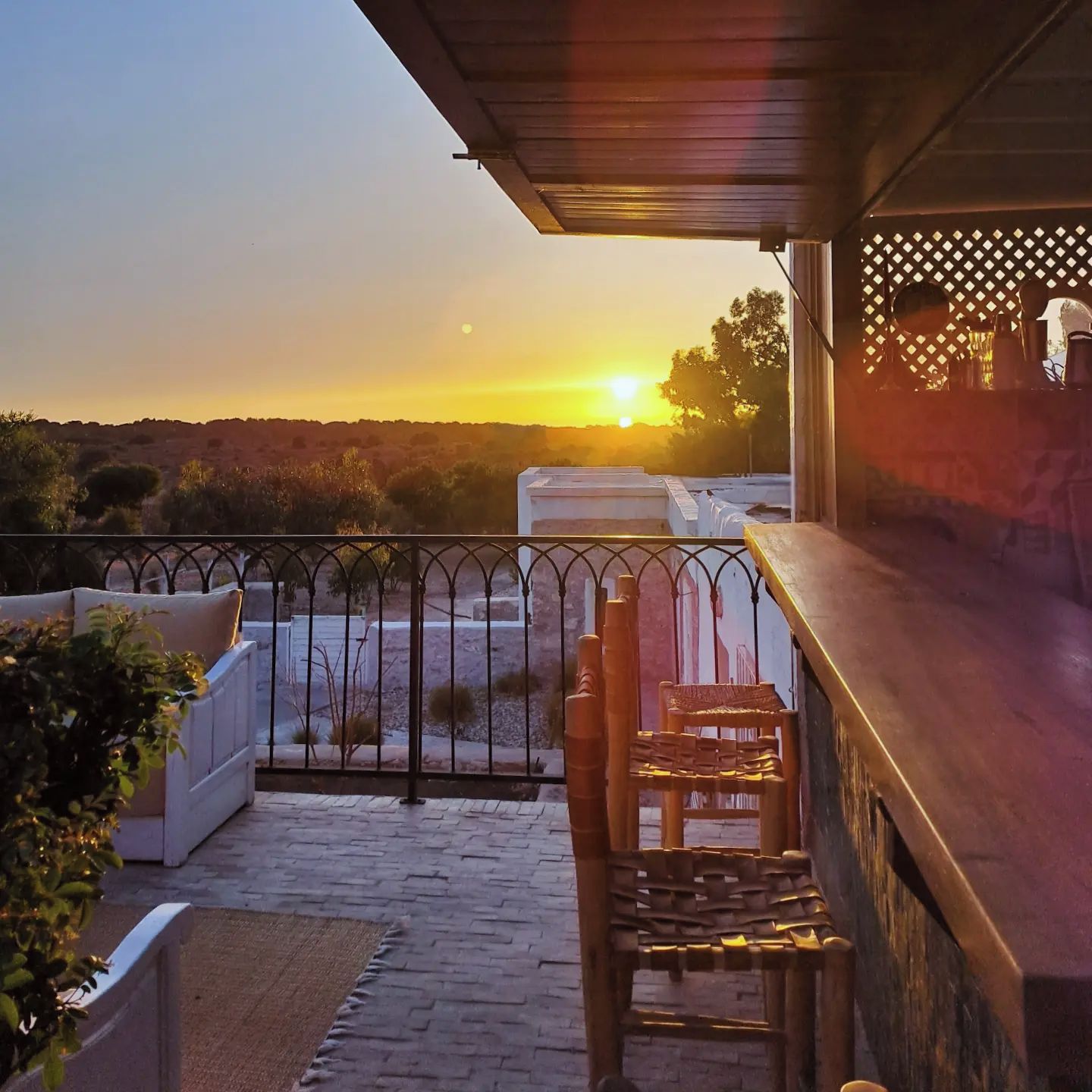 Ein Balkon mit Blick auf den Sonnenuntergang, ein Holzsessel und eine weiße gepolsterte Bank.