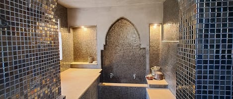 Et badeværelse med vægge af mosaikfliser, et badekar og et bruseområde.