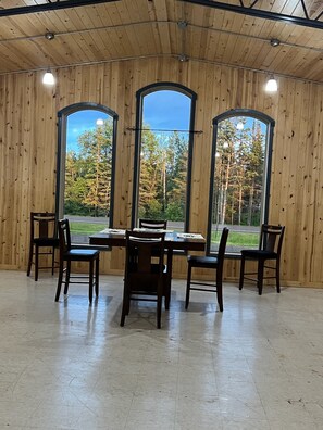 Ein Essbereich mit Holzvertäfelung, einem Tisch mit Stühlen und großen Fenstern mit Blick auf Bäume und eine Straße.