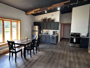 Una cocina moderna con armarios oscuros, un refrigerador de acero inoxidable y un comedor con una mesa y sillas de madera.