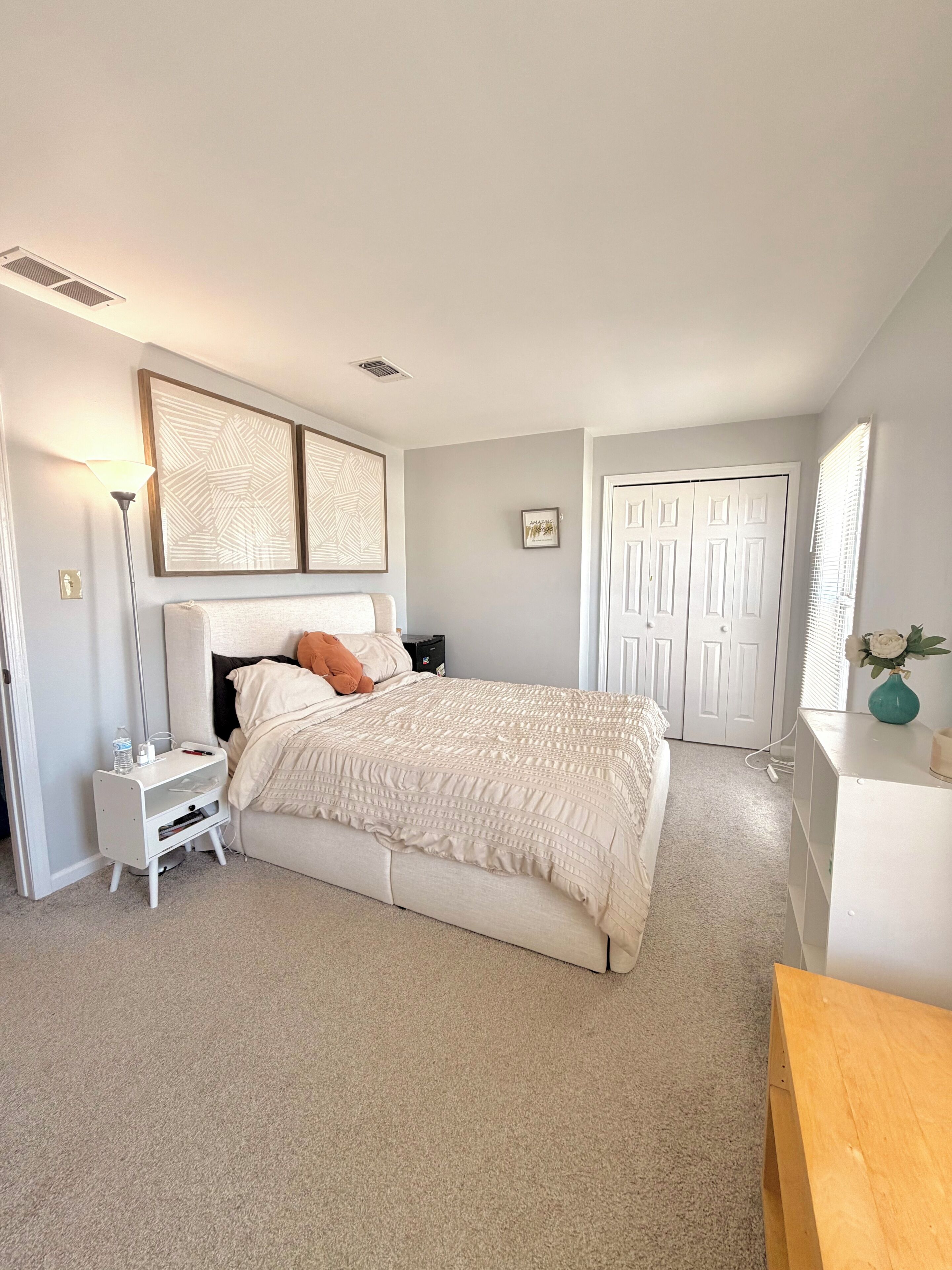 Un dormitorio con cama, mesitas de noche, lámpara, puerta y espejo.
