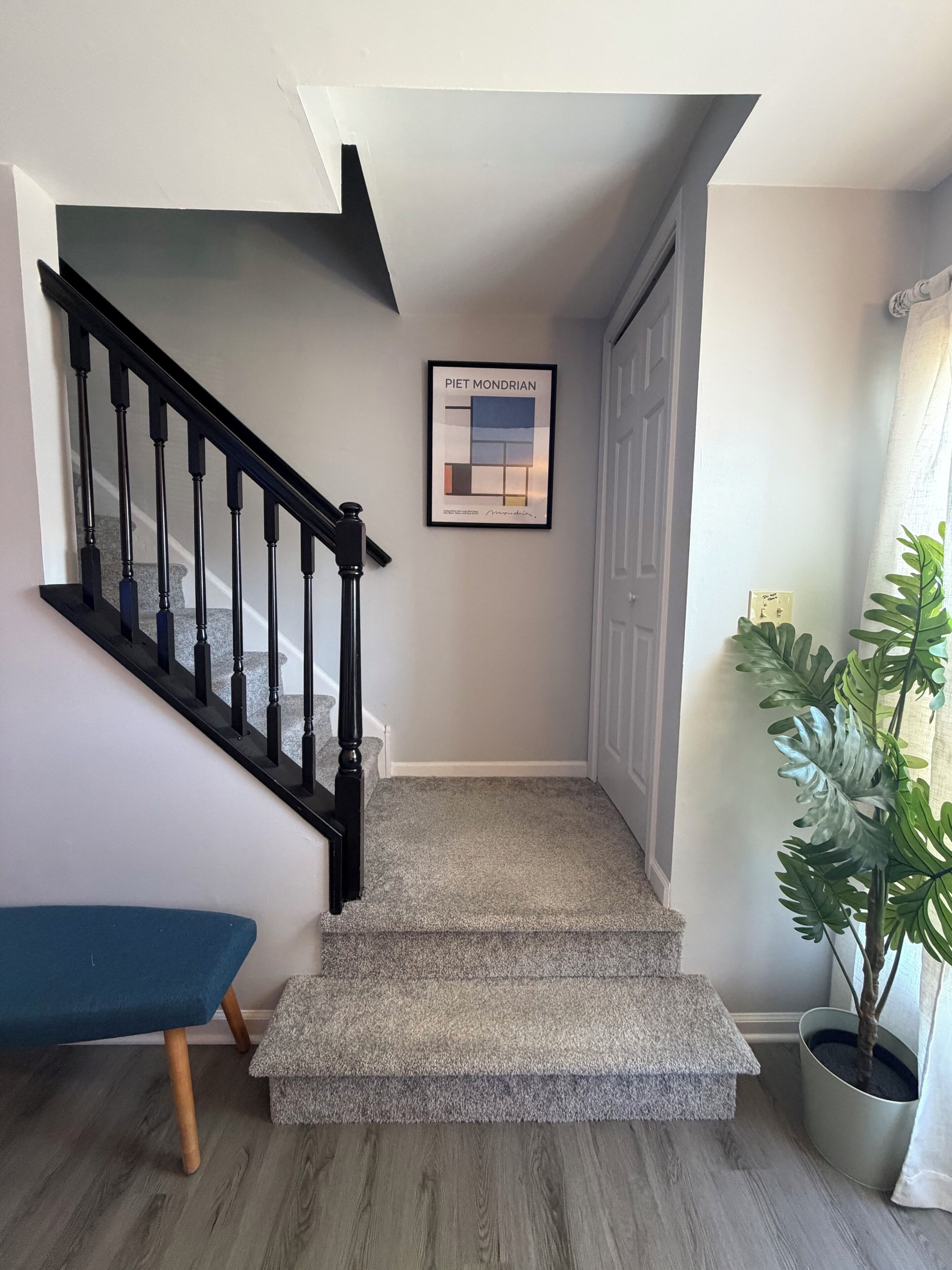Un escalier dont les marches sont recouvertes de moquette, avec une rampe noire et une œuvre d’art encadrée accrochée au mur.