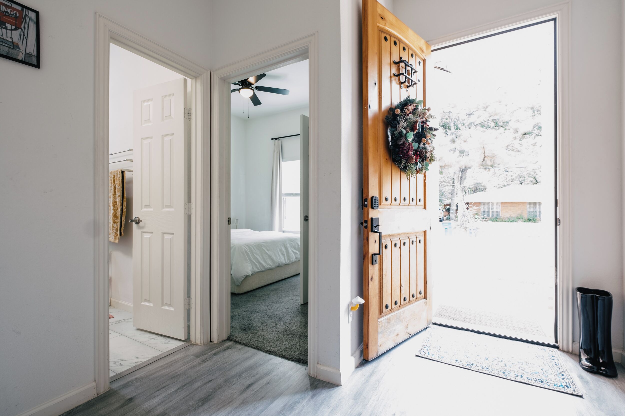 Un couloir menant à une chambre à coucher équipée d’un lit, d’un ventilateur de plafond et d’une porte ornée d’une guirlande.