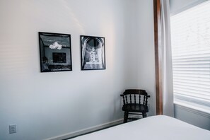 A bedroom with a bed, a chair, and two framed pictures on the wall.