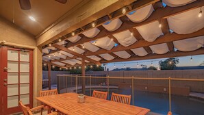 An outdoor patio with a wooden table and chairs, a pool, and a pergola with string lights. - Scottsdale 4-bedroom house with pool and hot tub. (Scottsdale)