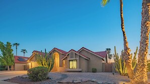 A residential building with a red-tiled roof, a central entrance with a door, and a small porch. There are cacti and a palm tree in the foreground. - Scottsdale 4-bedroom house with pool and hot tub. (Scottsdale)