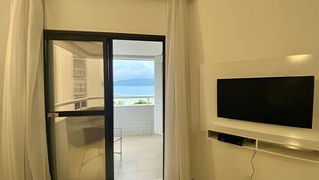 Quarto com porta de vidro deslizante que dá para uma varanda com vista para o mar. Uma televisão de tela plana está fixada na parede.