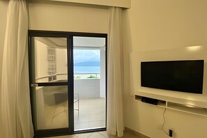 Una habitación con puerta de cristal corredera que da a un balcón con vista al mar. Un televisor de pantalla plana está montado en la pared.