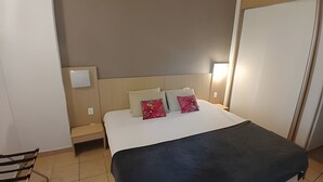 Una habitación de hotel con una cama, dos mesitas de noche, una silla y una puerta.