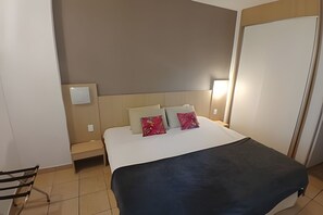 Una habitación de hotel con una cama, dos mesitas de noche, una silla y una puerta.