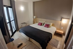 A hotel room with a bed, bedside tables, a small table with a remote control, and a chair. - SHB - Flat vista mar no Boqueirão (Santos)