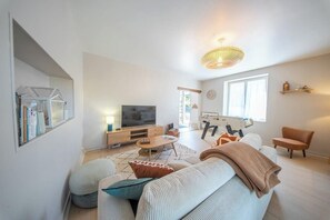 Ein modernes Wohnzimmer mit Fernseher, Sofa, Couchtisch und einem großen Fenster.