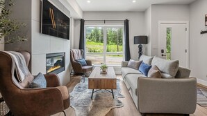 Un salon moderne doté d’une cheminée, de sièges confortables, d’une table basse et d’une grande fenêtre donnant sur un paysage verdoyant.