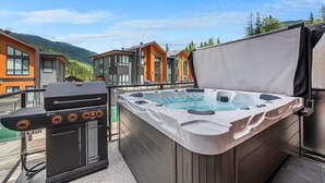 Un bain à remous sur une terrasse extérieure, avec vue sur des bâtiments modernes et des montagnes en arrière-plan.