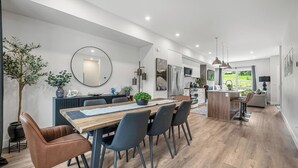 Une cuisine moderne avec un îlot central, un coin repas doté d’une table et de chaises en bois, et un grand miroir au mur.