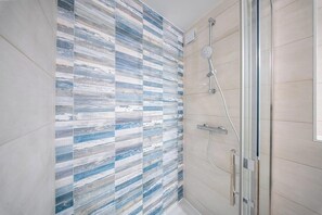 Eine Dusche mit Glastür, eine Fliesenwand mit blau-weißem Muster und ein heller Boden.