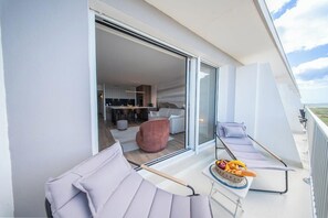 Ein Balkon mit zwei gepolsterten Stühlen, einem Tisch mit Früchten und einer Flasche sowie Blick ins Innere.