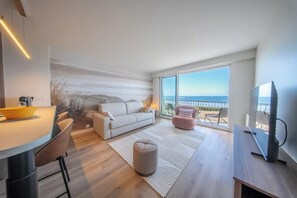 Ein modernes Wohnzimmer mit einer Couch, einem Hocker und einem Essbereich mit Tisch und Stühlen.