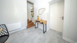 A modern interior with a wooden desk, a chair, a mirror, and a staircase leading to a room with shelves.