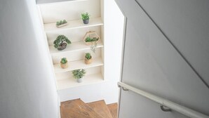 A staircase with wooden steps and white walls, leading to a landing with shelves holding potted plants.