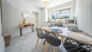 A modern kitchen with a dining area, a wooden table, black chairs, a hanging light fixture, and a window with a view.