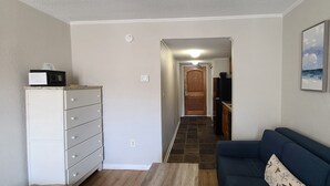 Un espacio habitable compacto con kitchenette, un sofá y una puerta que da a otra habitación.
