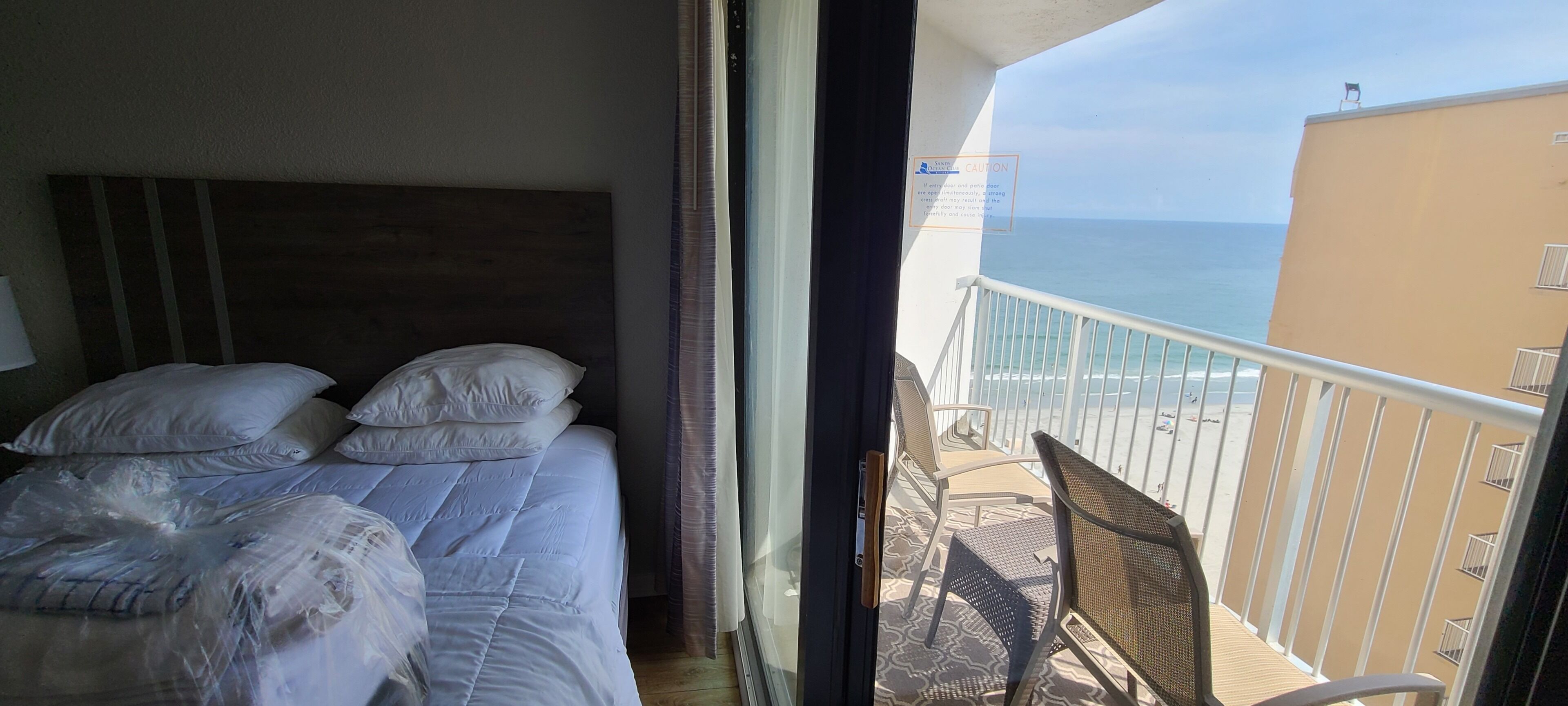 A hotel room with a bed, a window, and a balcony with a view of the sea.