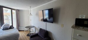Et hotelværelse med seng, fjernsyn hængt på væggen, et lille bord og en stol.