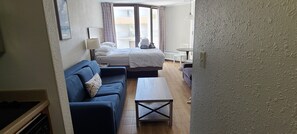 Habitación de hotel con cama, sofá, una mesita y vistas al exterior.