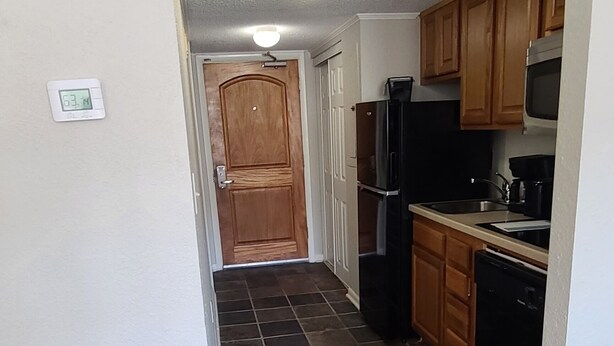 Una cocina con baldosas oscuras, armarios de madera y un refrigerador negro.