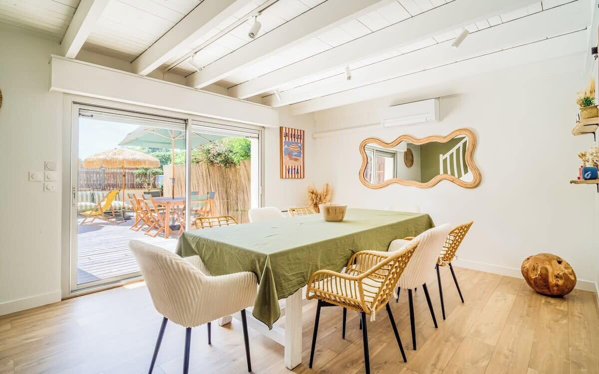 Un coin repas avec une table et des chaises, une porte-fenêtre coulissante donnant sur un espace extérieur et un miroir décoratif sur le mur.
