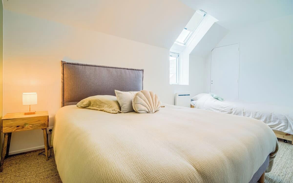 Quarto com cama grande, mesa de cabeceira, luminária, guarda-roupa e claraboia.