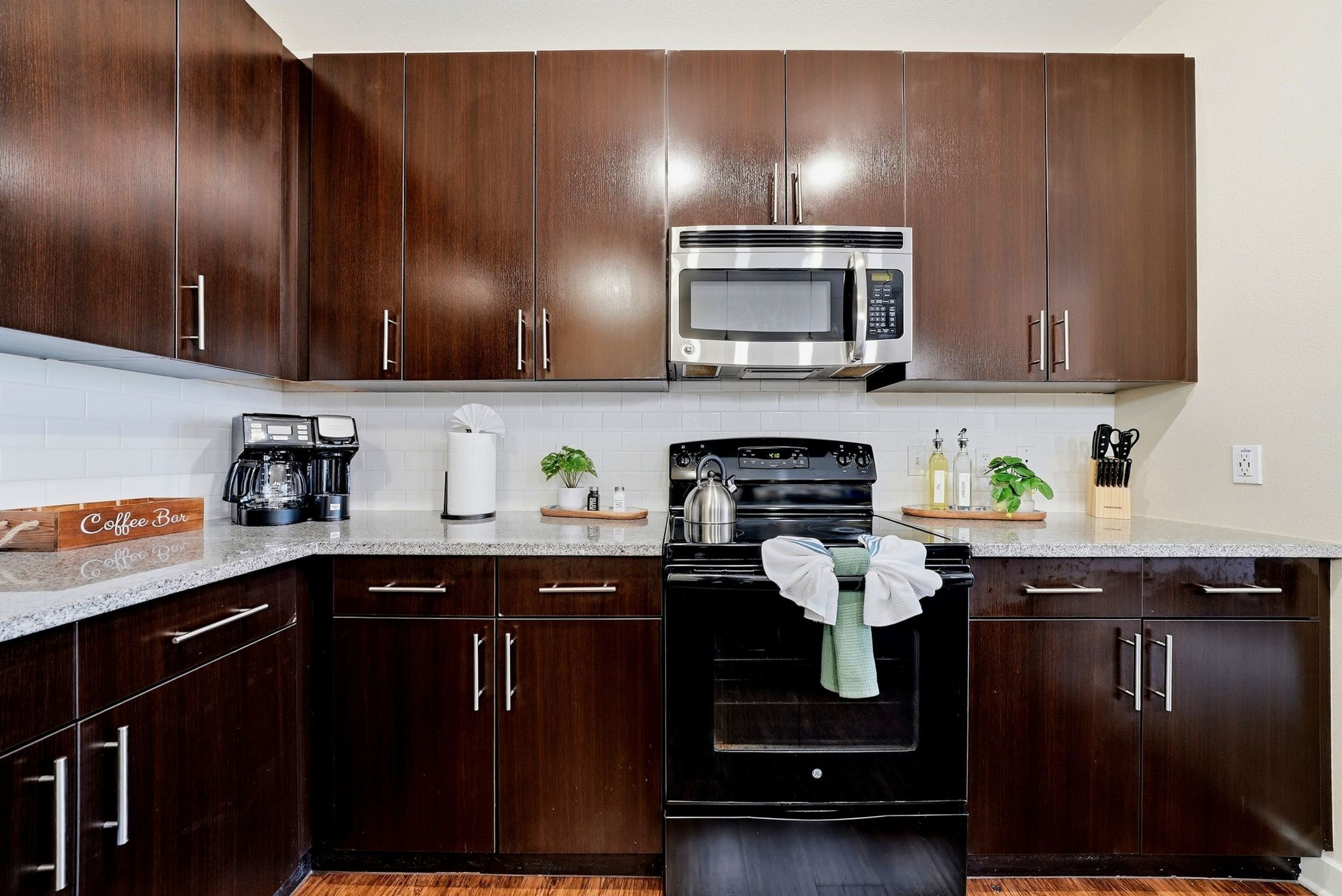 A kitchen with dark wood cabinets, a stainless steel microwave, a coffee maker, and a kettle.