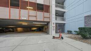 Un estacionamiento de varios niveles con un cartel de entrada visible, un letrero indicando zona de remolque, y una patineta roja estacionada afuera.